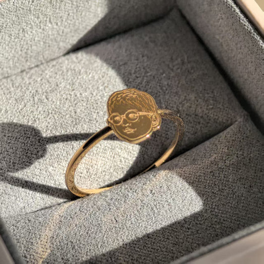 This image features a striking portrait ring, placed elegantly on a grey cushion. The ring is designed with a detailed and textured profile of a face, finely engraved on its band.